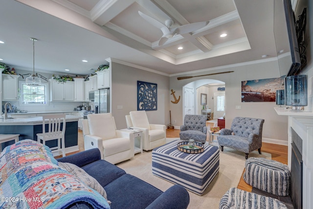 living room with coffered ceiling, ornamental molding, beamed ceiling, ceiling fan, and light hardwood / wood-style flooring