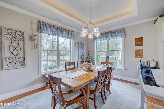 dining room featuring ornamental molding, light hardwood / wood-style flooring, a notable chandelier, and a tray ceiling