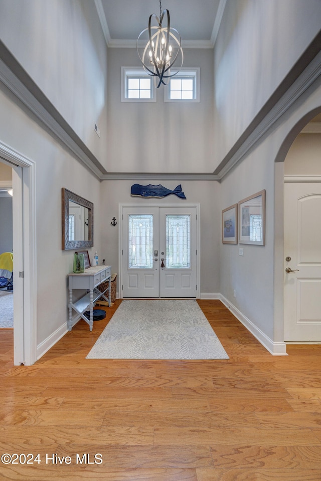 foyer featuring a high ceiling, light wood-type flooring, an inviting chandelier, and crown molding