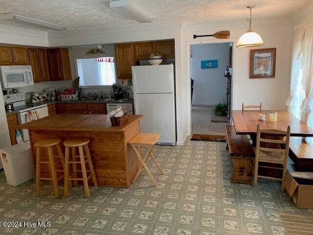 kitchen with white appliances, sink, a textured ceiling, hanging light fixtures, and a breakfast bar area