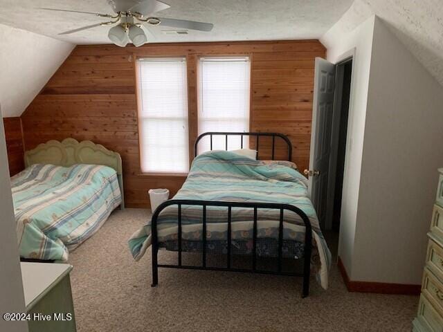 carpeted bedroom featuring ceiling fan, wood walls, a textured ceiling, and lofted ceiling