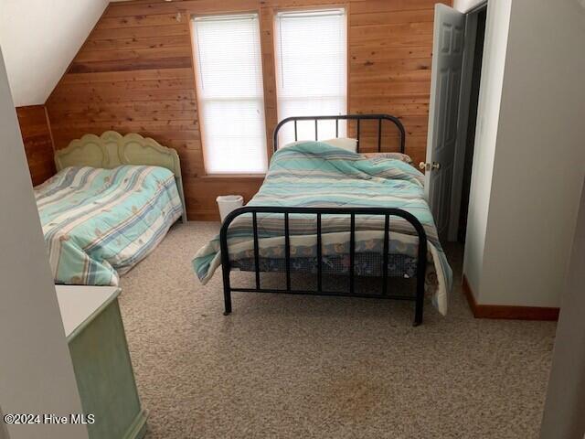 bedroom with carpet flooring, vaulted ceiling, and wooden walls