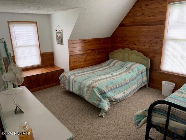 carpeted bedroom featuring vaulted ceiling, wood walls, and multiple windows