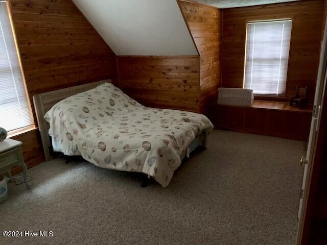 bedroom featuring multiple windows, wooden walls, carpet, and vaulted ceiling