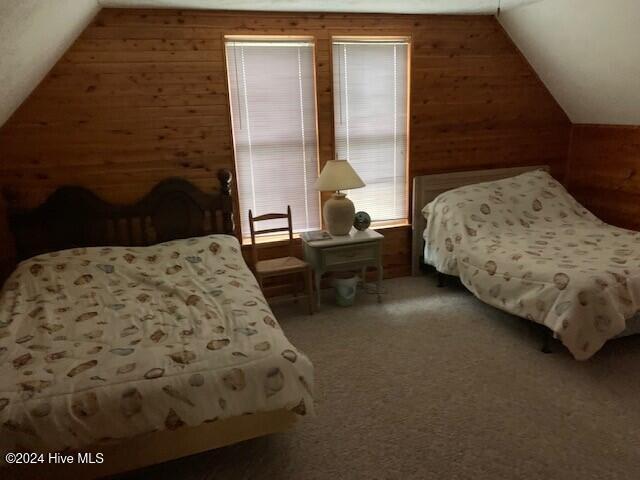 bedroom featuring wooden walls, vaulted ceiling, and carpet flooring