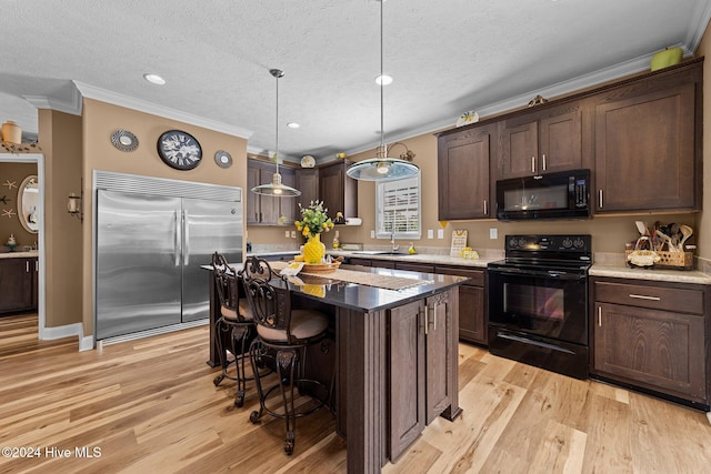 kitchen with a kitchen island, light wood-type flooring, ornamental molding, black appliances, and decorative light fixtures