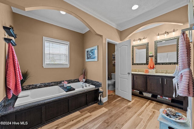 bathroom with hardwood / wood-style flooring, a tub, toilet, ornamental molding, and vanity