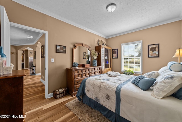 bedroom with crown molding, a textured ceiling, and light hardwood / wood-style flooring