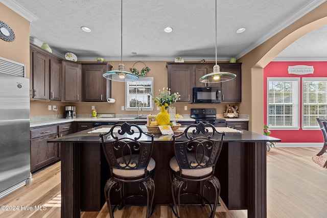 kitchen with black appliances, hanging light fixtures, light wood-type flooring, and a kitchen island