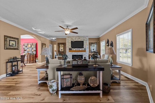 living room featuring light hardwood / wood-style floors, crown molding, a stone fireplace, and ceiling fan