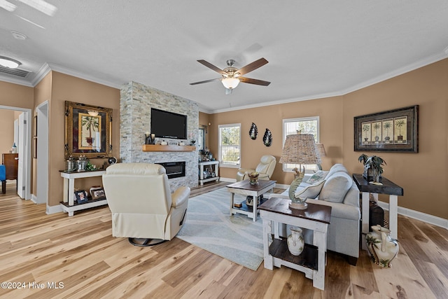 living room featuring light hardwood / wood-style floors, ornamental molding, a stone fireplace, and ceiling fan