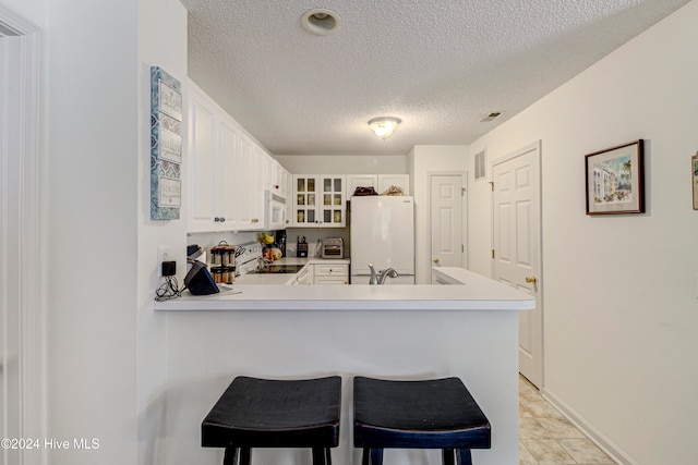 kitchen with kitchen peninsula, a breakfast bar, white cabinetry, a textured ceiling, and white appliances