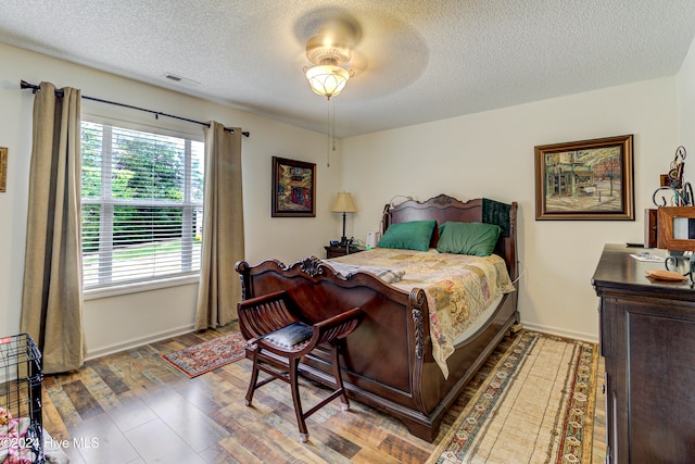 bedroom with a textured ceiling, light wood-type flooring, and ceiling fan