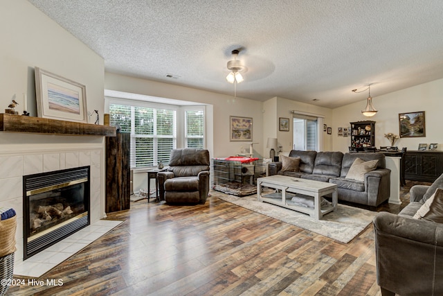 living room featuring a tiled fireplace, ceiling fan, a textured ceiling, vaulted ceiling, and light hardwood / wood-style floors