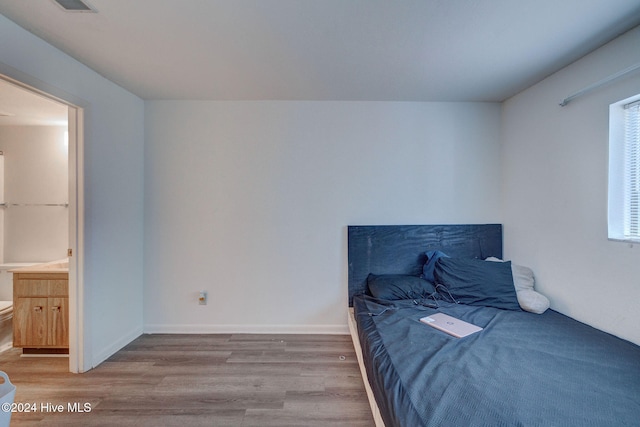 bedroom with connected bathroom, multiple windows, and wood-type flooring