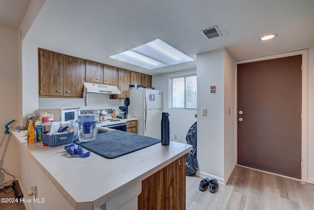 kitchen with light wood-type flooring, kitchen peninsula, and white appliances