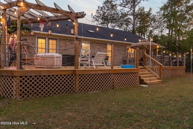 back house at dusk featuring a pergola, a hot tub, a lawn, and a wooden deck