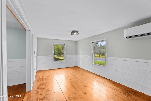 unfurnished room with a healthy amount of sunlight, an AC wall unit, and hardwood / wood-style flooring