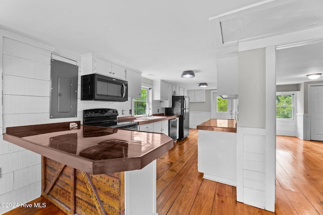 kitchen with kitchen peninsula, electric panel, white cabinetry, black appliances, and light hardwood / wood-style floors