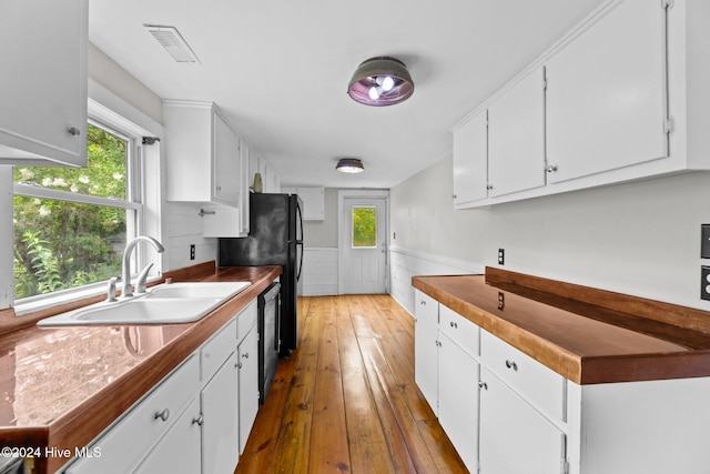 kitchen featuring black dishwasher, sink, white cabinets, and wood-type flooring