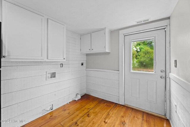 washroom featuring wood walls, hookup for an electric dryer, light hardwood / wood-style floors, washer hookup, and cabinets