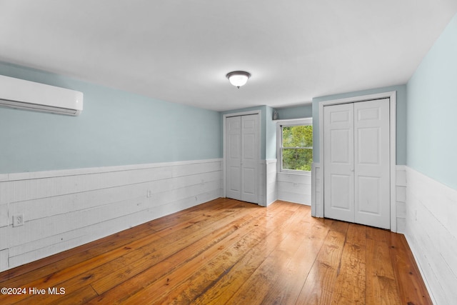 unfurnished bedroom with a wall unit AC, two closets, and light hardwood / wood-style floors