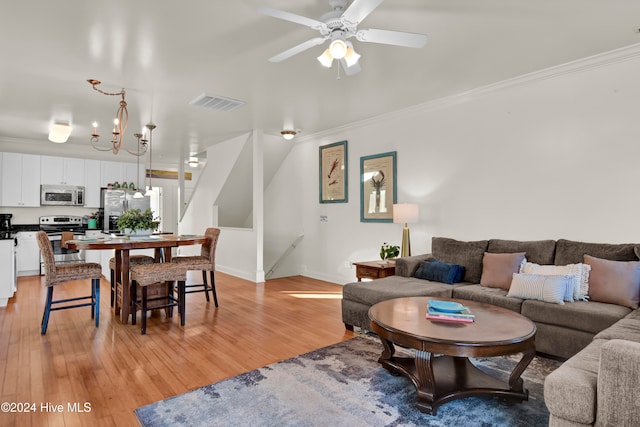 living room featuring ceiling fan with notable chandelier, light wood-type flooring, and crown molding