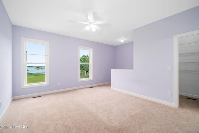 empty room with a water view, ceiling fan, and light colored carpet