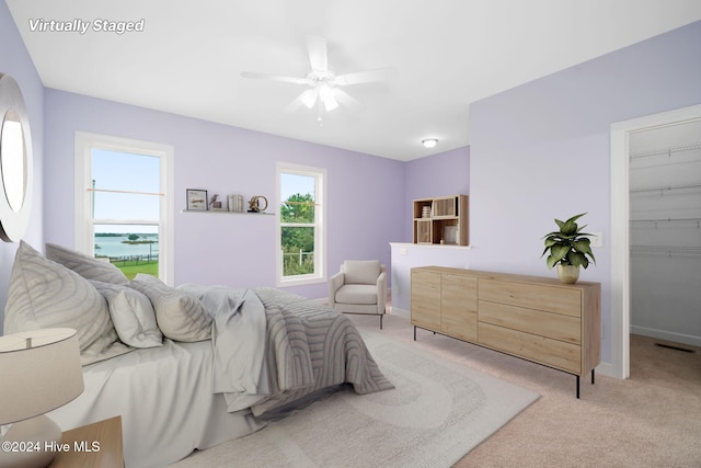 bedroom featuring ceiling fan, light colored carpet, a walk in closet, a closet, and a water view