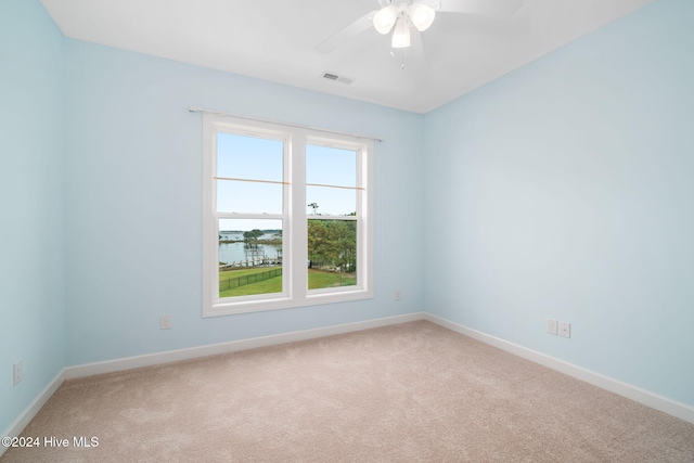 carpeted empty room with a water view and ceiling fan