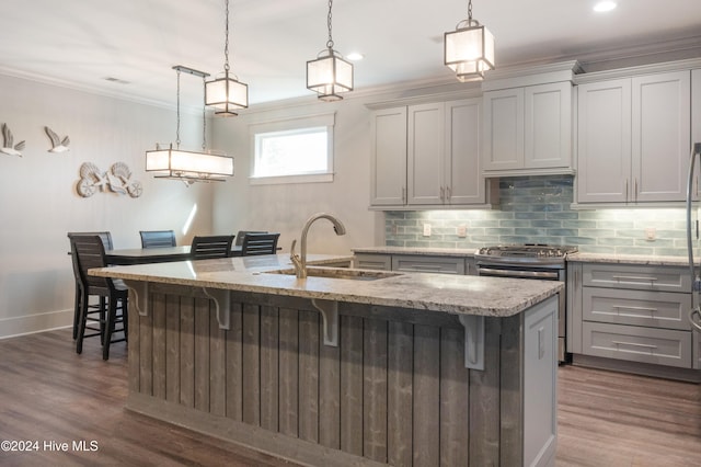 kitchen featuring a breakfast bar area, a kitchen island with sink, decorative light fixtures, and dark hardwood / wood-style flooring