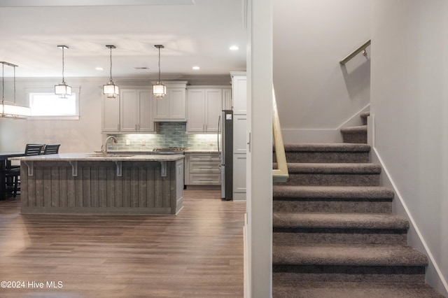 kitchen with sink, a kitchen bar, dark hardwood / wood-style flooring, decorative light fixtures, and a center island with sink