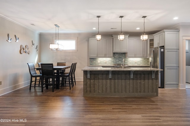 kitchen with a breakfast bar area, decorative light fixtures, dark wood-type flooring, and stainless steel refrigerator