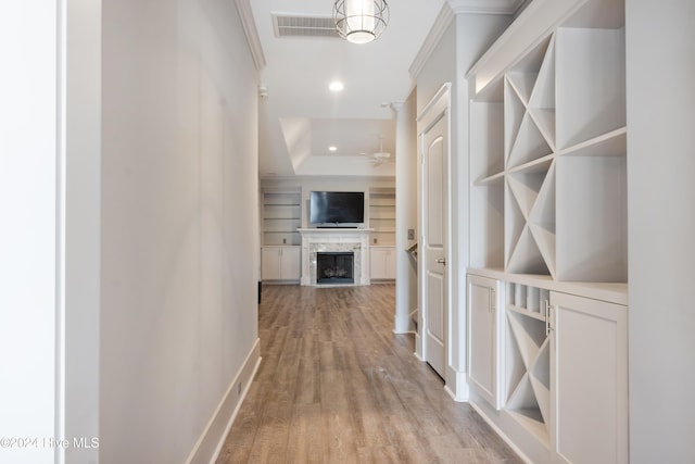 corridor featuring light hardwood / wood-style floors, crown molding, and built in features