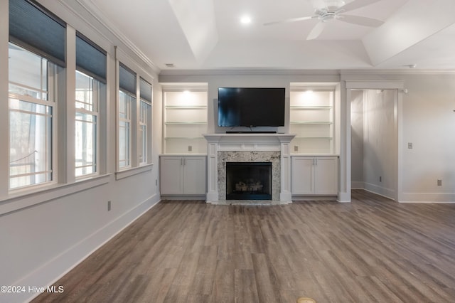 unfurnished living room featuring wood-type flooring, a tray ceiling, ornamental molding, a high end fireplace, and ceiling fan