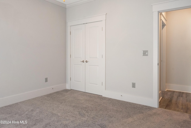 unfurnished bedroom featuring a closet, crown molding, and dark carpet