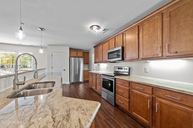 kitchen with appliances with stainless steel finishes, sink, decorative light fixtures, dark wood-type flooring, and light stone counters