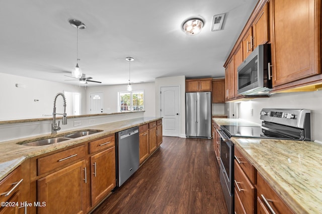 kitchen featuring light stone countertops, sink, stainless steel appliances, decorative light fixtures, and dark wood-type flooring