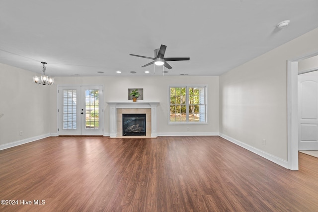 unfurnished living room featuring ceiling fan with notable chandelier, dark hardwood / wood-style floors, a tile fireplace, and plenty of natural light