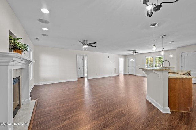 unfurnished living room with ceiling fan, sink, a tile fireplace, and dark hardwood / wood-style flooring