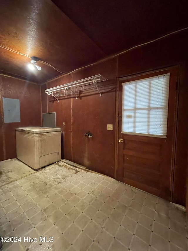 clothes washing area with electric panel and wooden walls