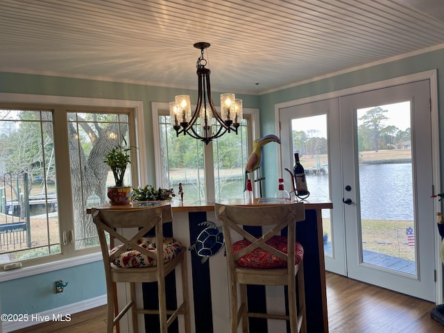 dining area featuring a water view, wood finished floors, baseboards, french doors, and ornamental molding