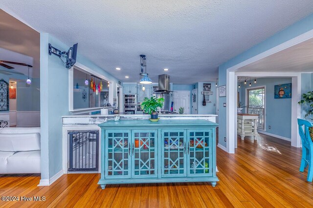 interior space with a textured ceiling, stainless steel double oven, wood finished floors, baseboards, and ventilation hood