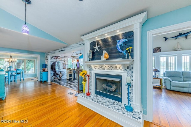 living area featuring visible vents, a tile fireplace, lofted ceiling, wood-type flooring, and an inviting chandelier