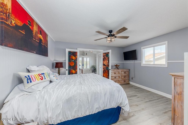 bedroom with a textured ceiling, ceiling fan, multiple windows, and wood finished floors