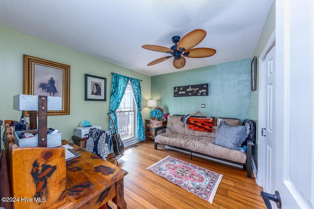 living room featuring hardwood / wood-style flooring, visible vents, a ceiling fan, and a textured ceiling