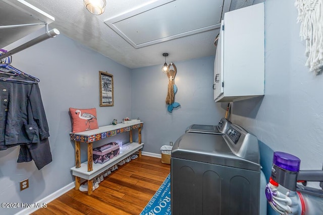 clothes washing area featuring washer and clothes dryer, cabinet space, attic access, wood finished floors, and baseboards