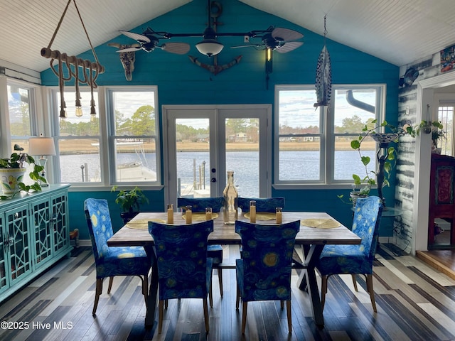 dining space featuring lofted ceiling, a water view, wood finished floors, a ceiling fan, and french doors