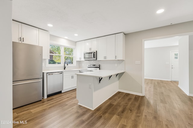 kitchen featuring white cabinetry, appliances with stainless steel finishes, light hardwood / wood-style flooring, and kitchen peninsula