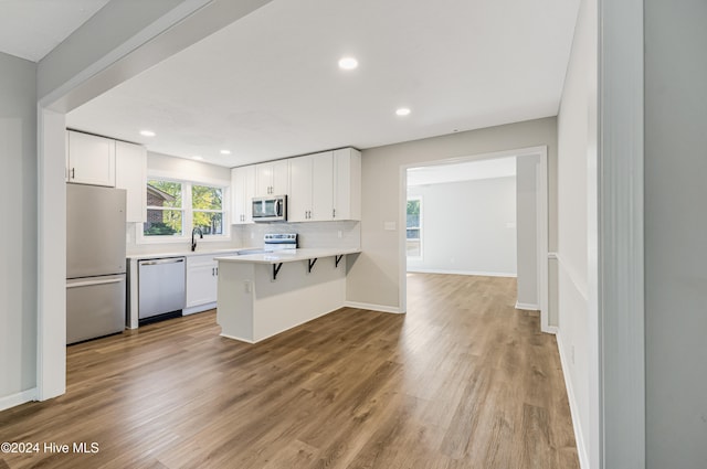 kitchen with appliances with stainless steel finishes, light hardwood / wood-style flooring, a kitchen bar, and white cabinets